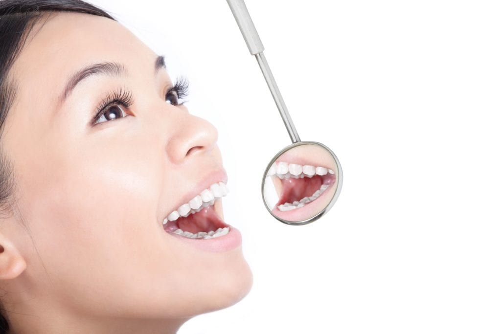 woman opening her mouth and using a dental mirror
